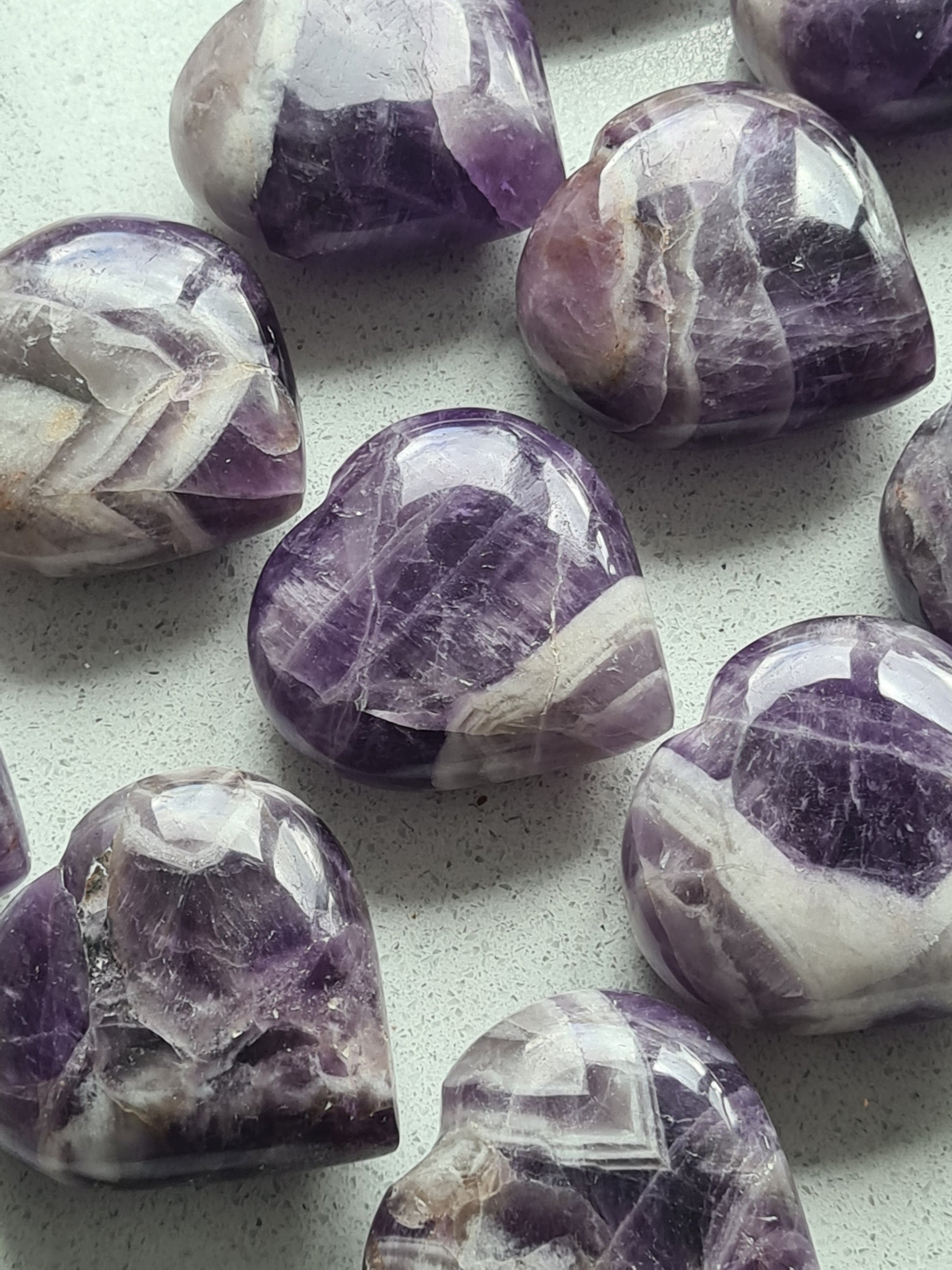 A collection of Dream Amethyst Polished Hearts, displaying purple and white banding. Intuitively chosen.